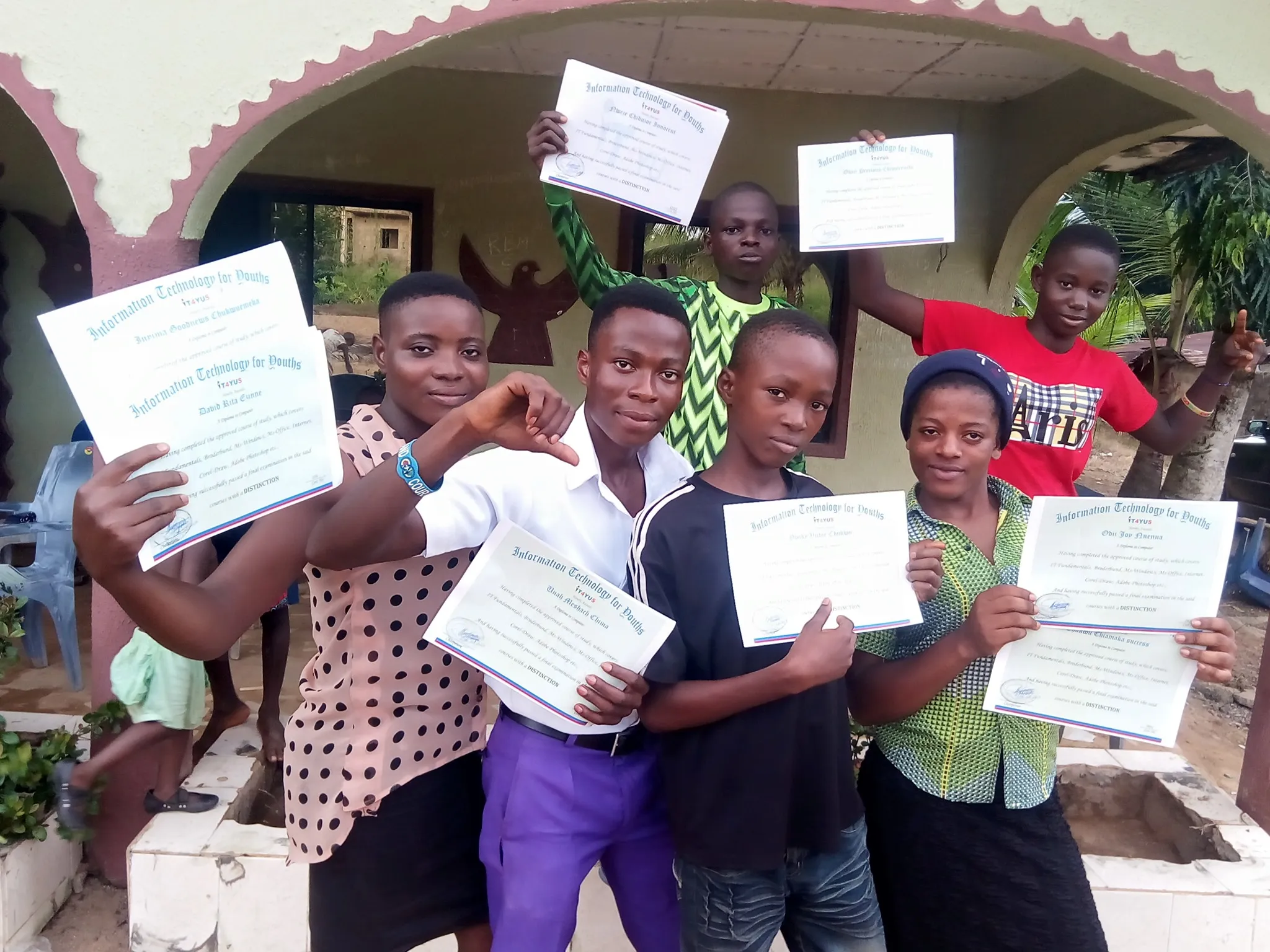 Students hold up their IT4YUS training certificates outside a building