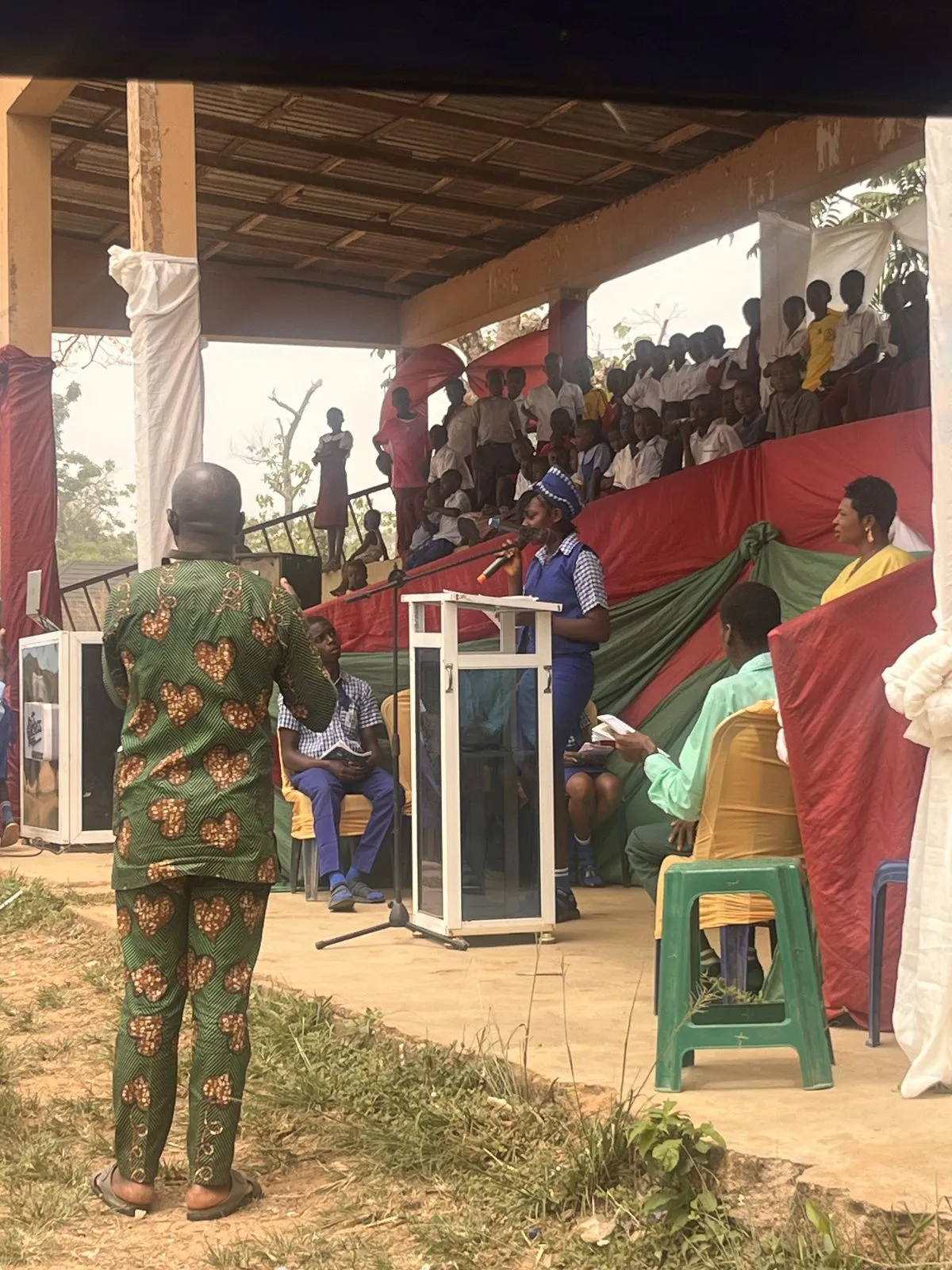 A guest in traditional dress watches from the floor as students fill the covered stands, 2026