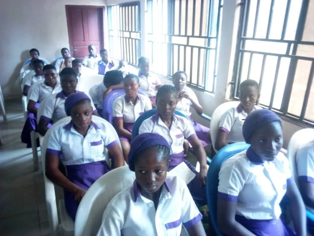 Students in purple and white uniforms watch from the audience