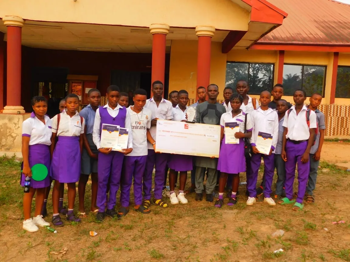 Debate participants in purple uniforms hold certificates and a cheque outside the hall