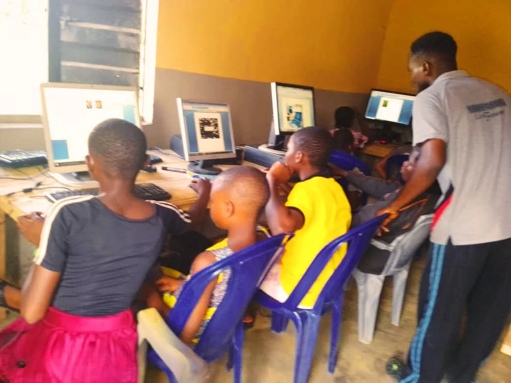 A trainer helps young students at a row of computers