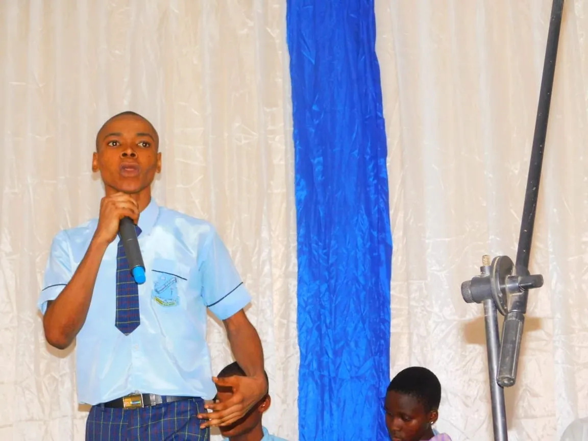 A student in a light blue shirt and tie addresses the audience