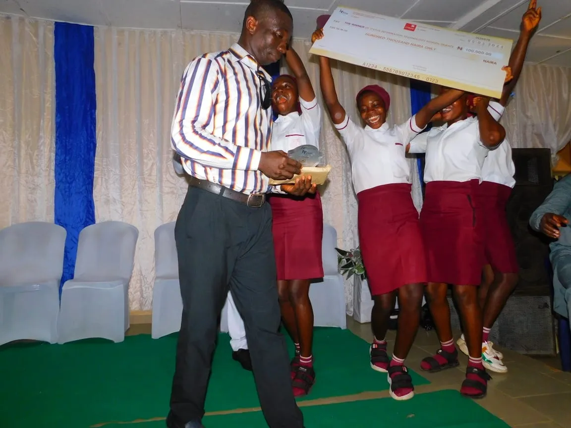Students leap and cheer holding the winners' cheque on stage at the 2024 IT Debate